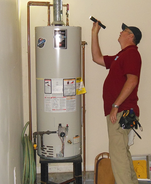 Man inspecting a water heater with a flashlight.
