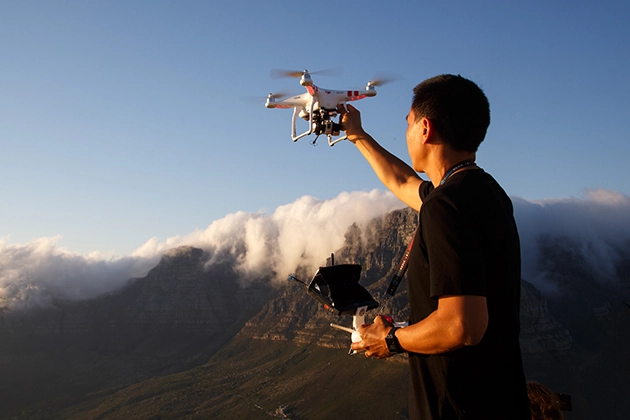 Man operating drone with mountain landscape in the background.