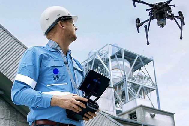 Man in safety gear operating a drone near industrial facility.